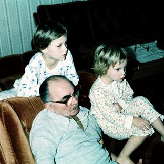 Family sitting indoors, grandfather with two grandchildren.