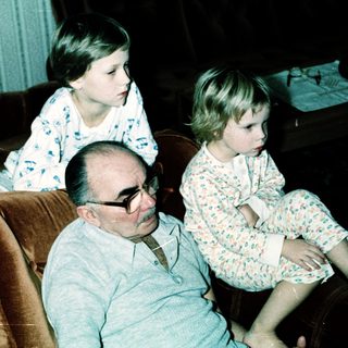Family sitting indoors, grandfather with two grandchildren.