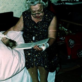 Two children lying on bed, an adult reading to them.