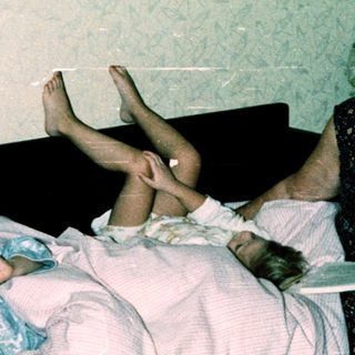 Two children lying on bed, an adult reading to them.