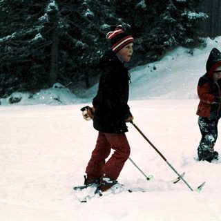 Two children skiing in snowy forest.