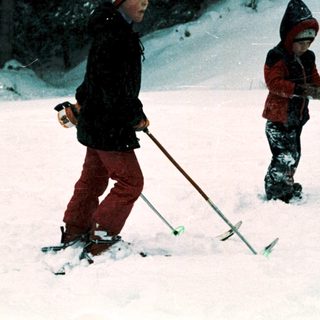 Two children skiing in snowy forest.