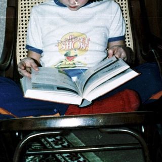 Child reading book with headphones in cozy chair.