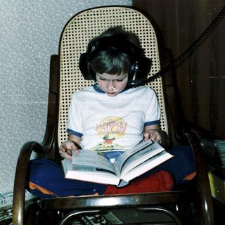 Child reading book with headphones in cozy chair.