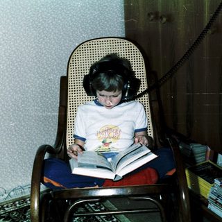 Child reading book with headphones in cozy chair.