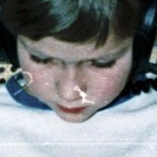 Child reading book with headphones in cozy chair.