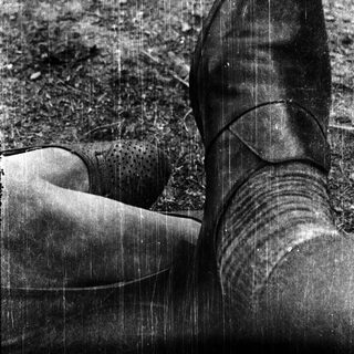 A person's feet in wet rain boots on muddy ground.