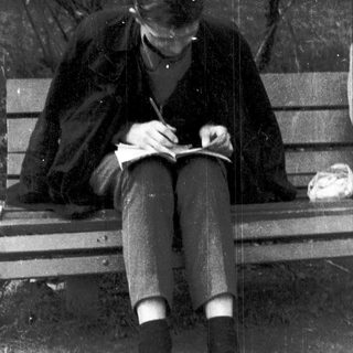 Person writing in notebook outdoors on bench.
