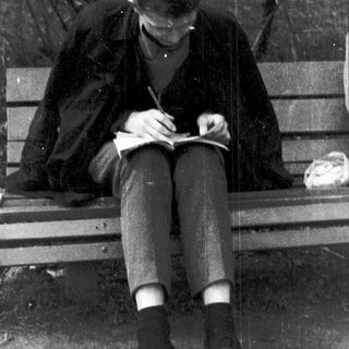 Person writing in notebook outdoors on bench.