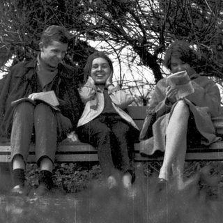 Three people sitting together outdoors, reading and smiling.