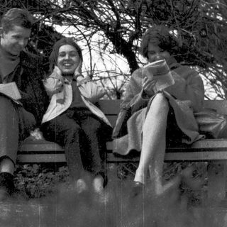Three people sitting together outdoors, reading and smiling.
