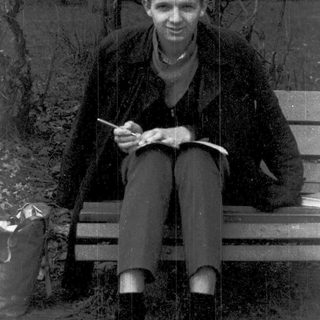 Young man sitting outdoors, sketching on a bench.