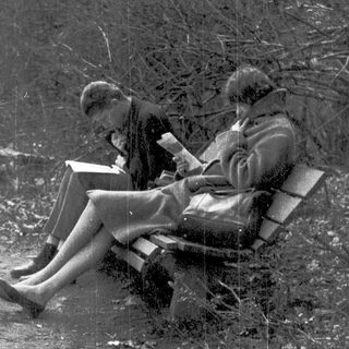 Two seated figures reading books outdoors.