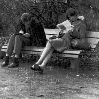 Two people reading books on a park bench.