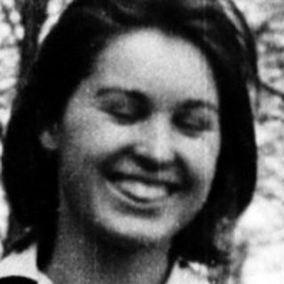 Young woman smiling outdoors in casual 1960s-style clothing.