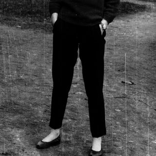 Young woman smiling outdoors in casual 1960s-style clothing.