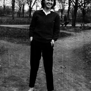 Young woman smiling outdoors in casual 1960s-style clothing.