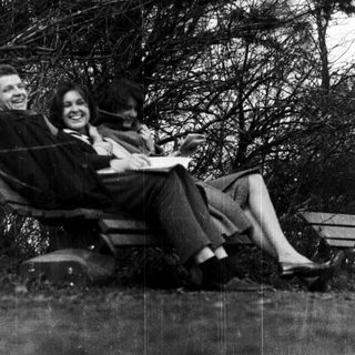 Three people smiling together outdoors on park bench.