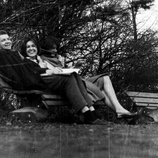 Three people smiling together outdoors on park bench.