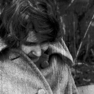 A person in vintage clothing gazing downward outdoors.