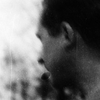 Man smoking outdoors near blurred greenery.