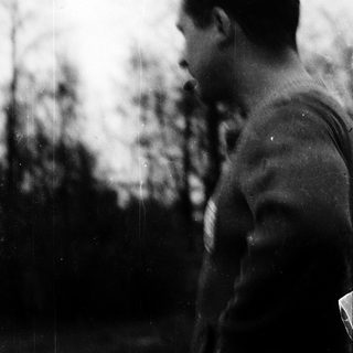 Man smoking outdoors near blurred greenery.