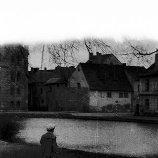 A lone person walks near a canal with historic buildings.