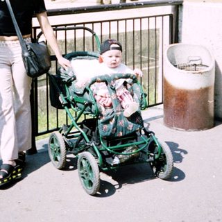 Two women and a baby in a stroller near an elephant enclosure.