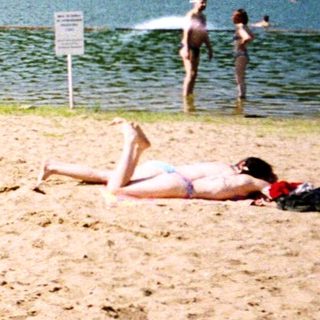 Sunny lake beach with people swimming and relaxing.