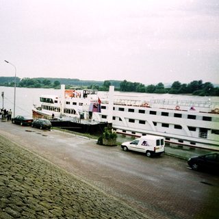 Riverfront ferry terminal with docked passenger boats and waiting vehicles.