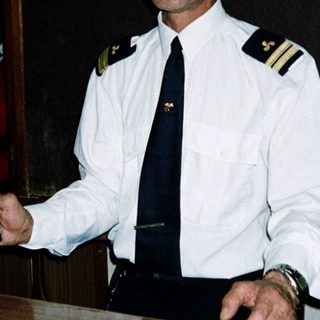 Maritime officer holding beverage at ship reception desk.