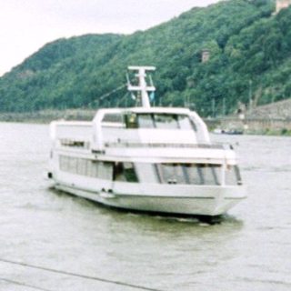 River scene with ferryboat, castle on hill, and dockside signs.