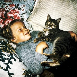 Child hugging a gray tabby cat indoors.