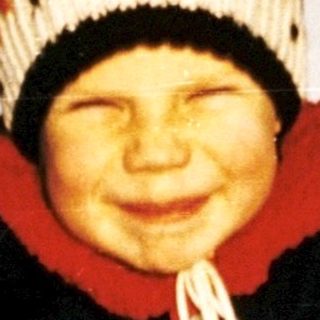 Child smiling on frozen lake with sled.