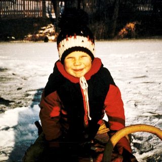 Child smiling on frozen lake with sled.