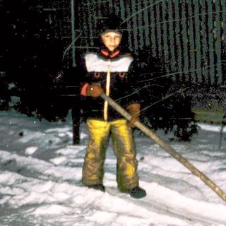Person shoveling snow at night near fenced building.