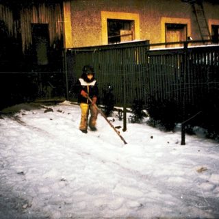 Child shoveling snow in residential yard at night.