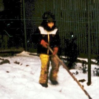 Child shoveling snow in residential yard at night.