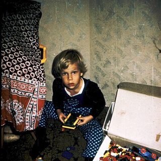 Child playing with open Lego box on carpet.