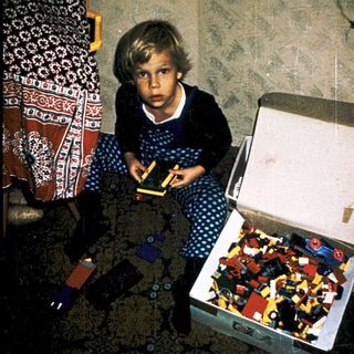 Child playing with open Lego box on carpet.