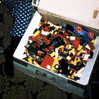 Child playing with open Lego box on carpet.