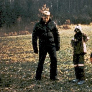 Family posing outdoors in rural field with forest background.