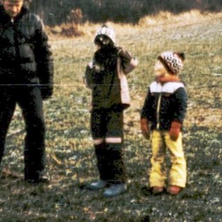 Family posing outdoors in rural field with forest background.