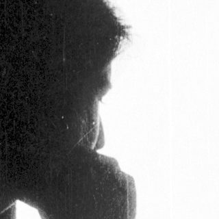 Two people sitting indoors, one resting chin on hand.