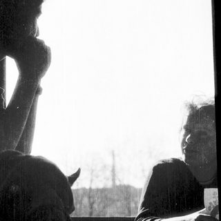 Two people sitting indoors, one resting chin on hand.