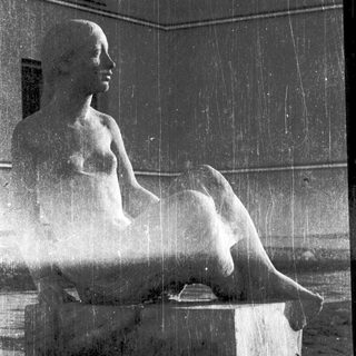 Seated classical statue under cascading fountain water.