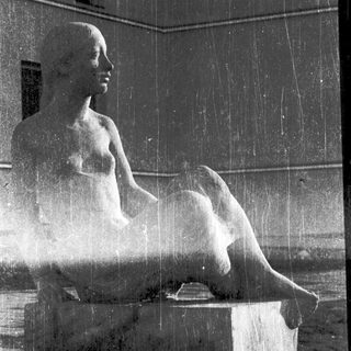 Seated classical statue under cascading fountain water.