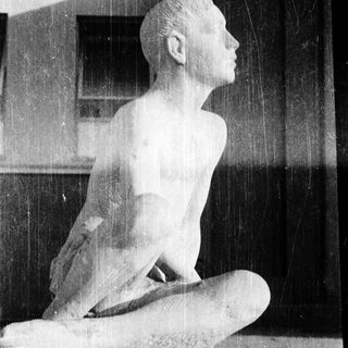 Sculpture of kneeling, head-in-hand figure outdoors.