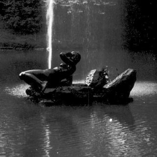 A statue of a child in a boat under a fountain.
