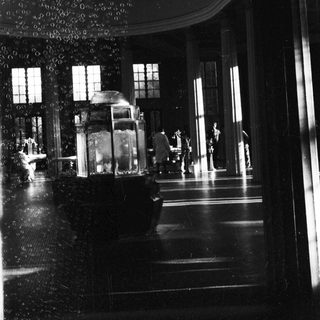 Vintage interior with grand staircase, ornate chandeliers, and dim lighting.